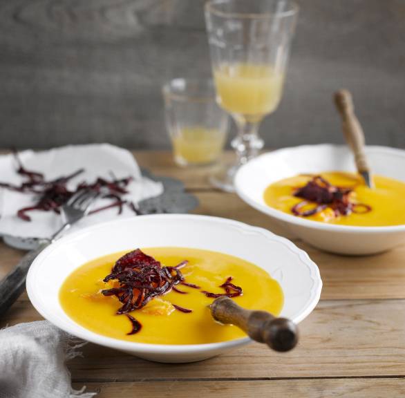 Selbstgekochte Kürbissuppe angerichtet auf zwei Supentellern mit frittierten Rote-Bete-Streifen