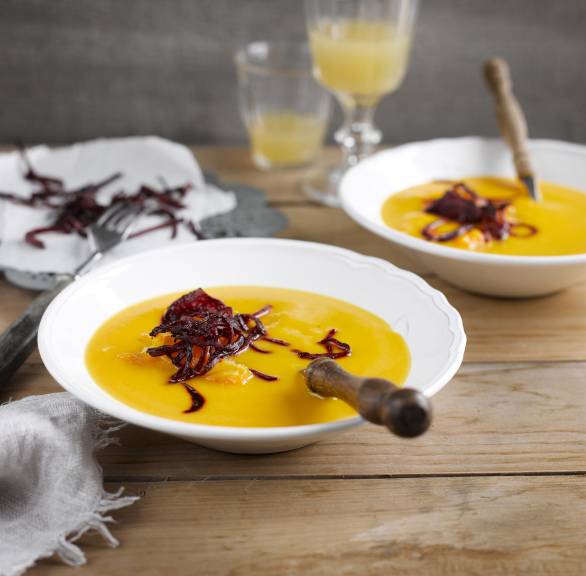 Selbstgekochte Kürbissuppe angerichtet auf zwei Supentellern mit frittierten Rote-Bete-Streifen