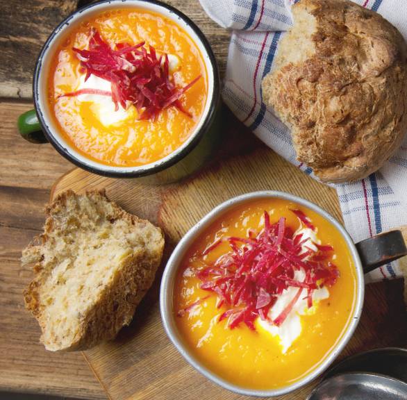 Kürbissuppe in zwei Suppenschüsseln auf einem Tisch, daneben Brot