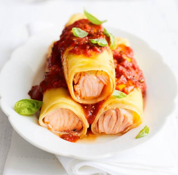 Drei Lachs-Canneloni gestapelt auf einem Teller, darauf Tomatensoße und Basilikum