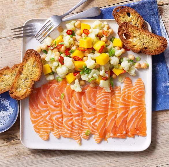 Lachs-Carpaccio angerichtet mit Blumenkohl-Mango-Salat und Brotchips auf einem Vorspeisenteller