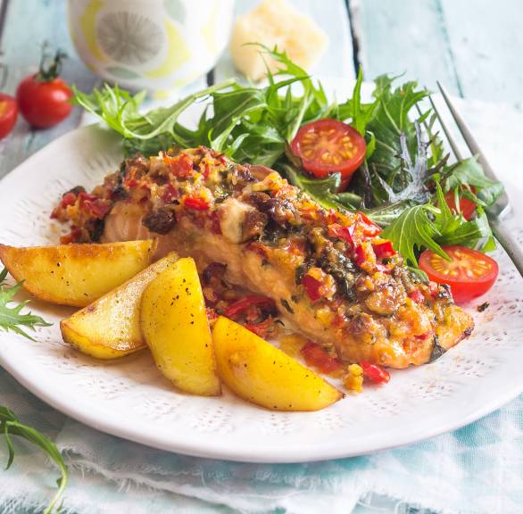 Ein Stück Ofenlachs mit Paprika-Pistazien-Kruste angerichtet mit Kartoffelspalten und Wildkräutersalat auf einem Teller