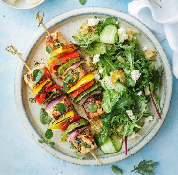 Gegrillte Lachs-Gemüse-Spieße auf einem Teller, daneben Salat und gegrillten Zitronen