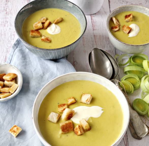 Lauchcremesuppe in mehreren Suppenschüsseln getoppt mit einem Klecks Crème fraîche und Croûtons auf einem Holztisch