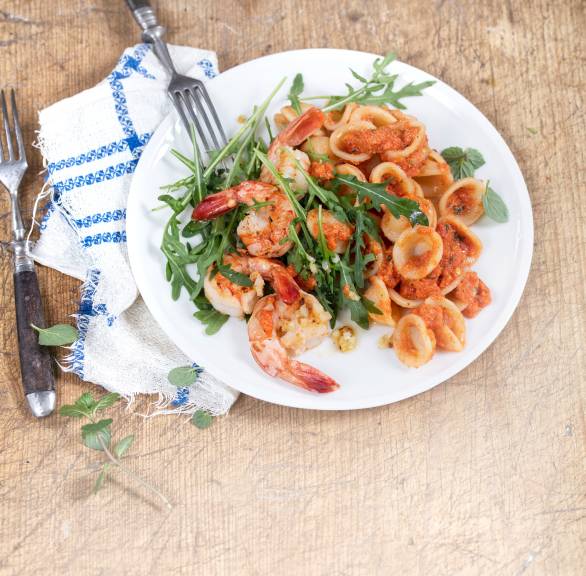 Nudelsalat mit Garnelen, Rucola und roter Sauce auf einem Teller