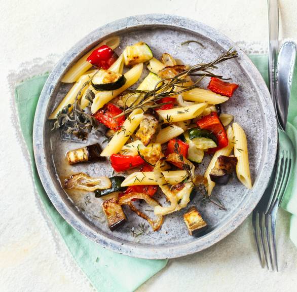 Nudelsalat mit Ofengemüse aus Zucchini, Aubergine und Paprika garniert mit Kräutern auf einem Teller