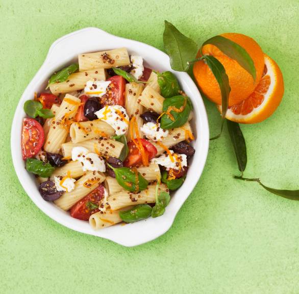 Nudelsalat in einer Schale mit Tomaten, Mozzarella und Basilikum, die Senfkörner des Dressings gut erkennbar