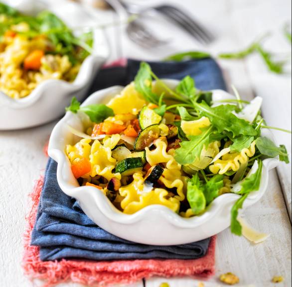 Nudelsalat mit Zucchini und Karotten, darauf Pistazien und Rucola in einer Salatschüssel auf einem Tisch