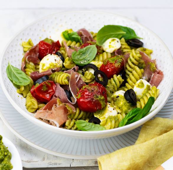Mediterraner, lauwarmer Nudelsalat mit Olivenpesto, Schinken und Ofentomaten angerichtet auf einem tiefen Teller