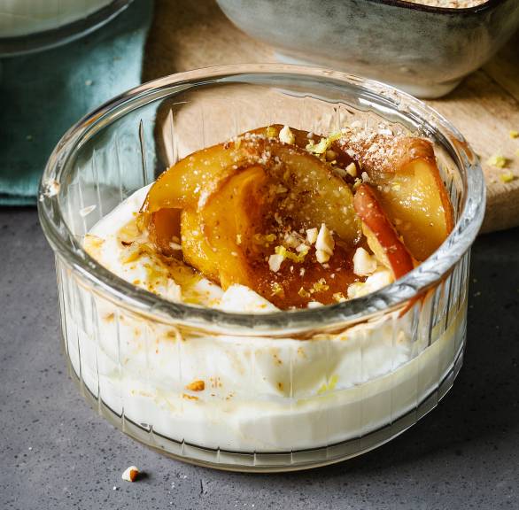 Limoncello-Mascarponedessert getoppt mit karamelliiserten Apfelspalten und Zitronen-Bröseln angerichtet in Dessertgläsern auf einem Tisch