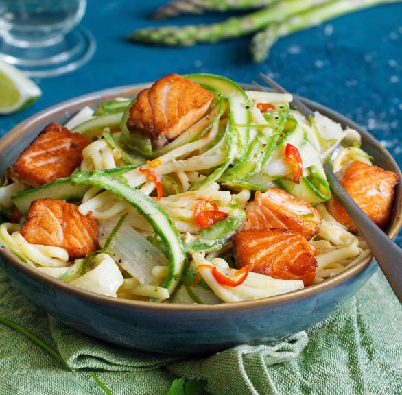 Spargelpasta mit Carbonara-Sauce und gebratenen Lachsstücken auf einem Teller