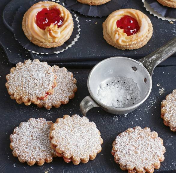 Linzer Plätzchen auf einer Schieferplatte, daneben Konfitüre und Puderzucker auf einem Tisch