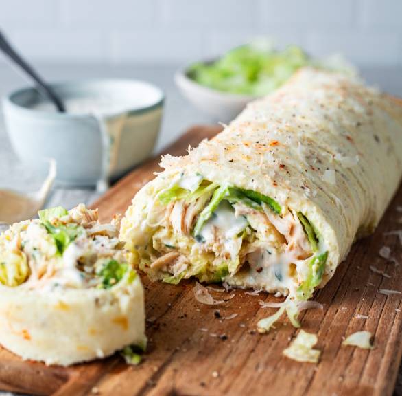 Low-Carb-Wrap aus Mozzarella, Ei und Quark angeschnitten mit Füllung aus Pute und Salat auf einem Holzbrett
