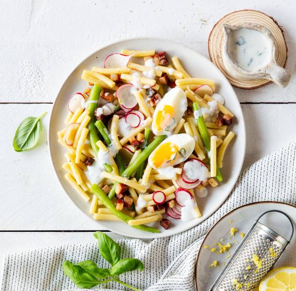 Nudelsalat aus Maccheroni mit Pancetta, Ei und grünen Bohnen auf einem Teller, daneben Joghurtdressing