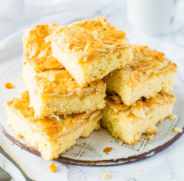 Mehrere Stücke Butterkuchen mit Mandeln vom Blech gestapelt auf einer Kuchenplatte