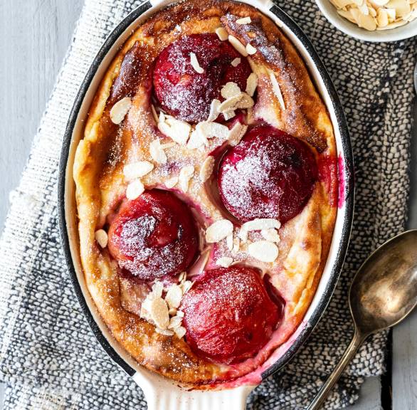 Mandelpudding in einer Auflaufform mit Pflaumen on top, daneben Mandelblättchen auf einem Tisch
