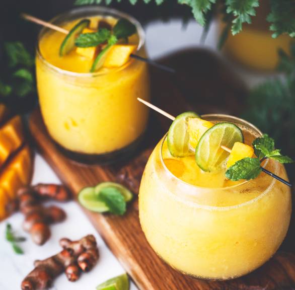 Gelber Smoothie mit Mango und Kurkuma in zwei Gläsern garniert mit Minze