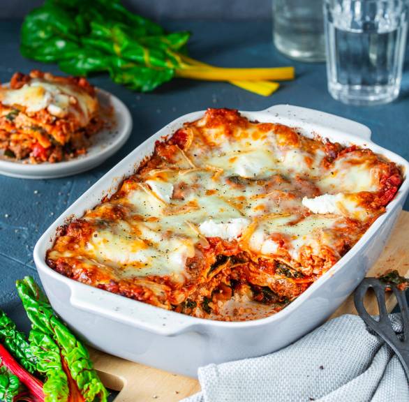 Mangoldlasagne mit Hackfleisch angeschnitten in einer Auflaufform, daneben Mangoldblätter