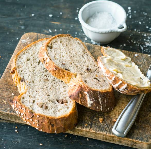 Scheiben von Sauerteigbrot auf einem Holzbrett, daneben Butter und Salz