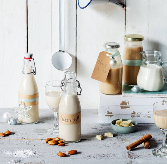 Marzipanlikör in Flaschen abgefüllt und mit Geschenkanhängern auf einem Holztisch