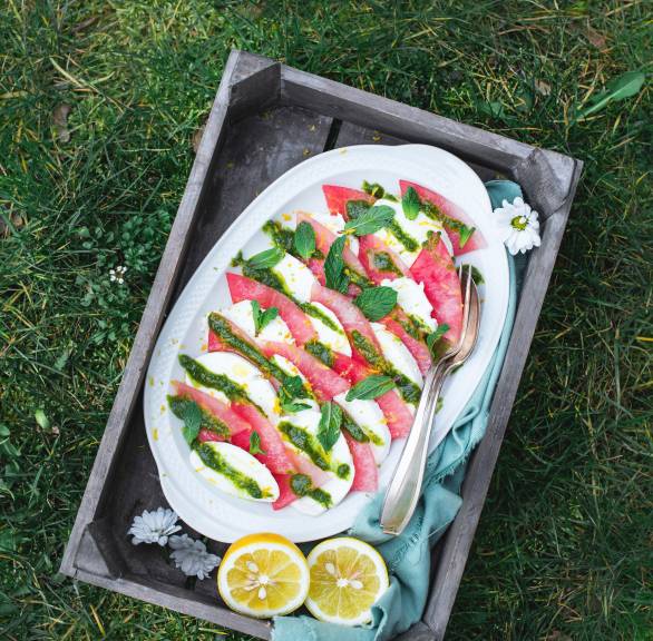 Caprese-Salat angerichtet auf einer weißen Platte aus Melonen- und Mozzarella-Streifen getoppt mit Pesto und Minze