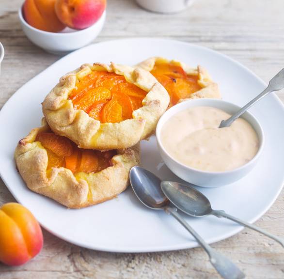 Mehrere  selbstgebackene Mini-Crostate mit Aprikosen angerichtet auf einem Teller, daneben Crème fraîche-Topping in einer Schale