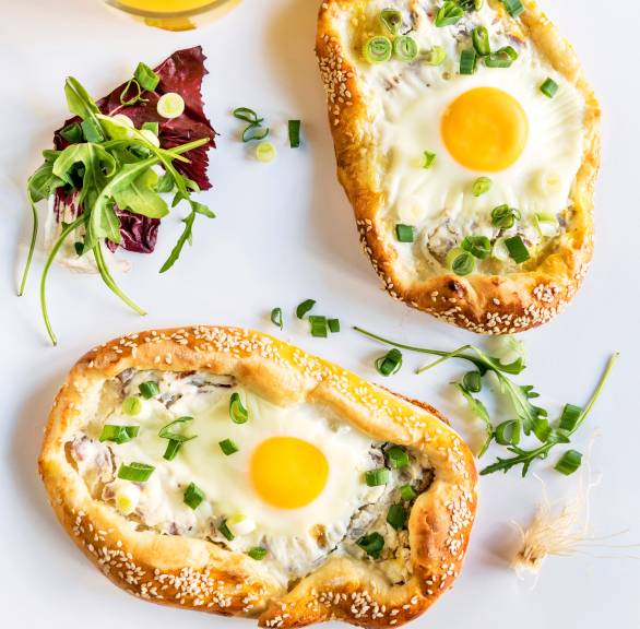 Zwei Minipizzen mit Eiern auf einem Tisch getoppt von frischen Kräutern