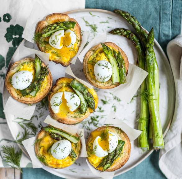Mehrere selbstgebackene Mini-Spargel-Quiches aus Blätterteig mit Wachteleiern angerichtet auf einer Servierplatte