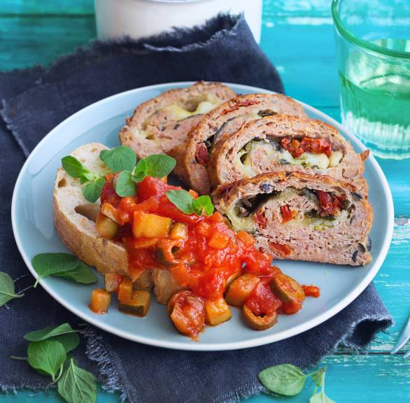 Vier Stücke Hackbraten mit Mozzarella-Gemüse-Füllung angerichtet auf einem Teller mit Ciabatta und Zucchini-Tomatensoße
