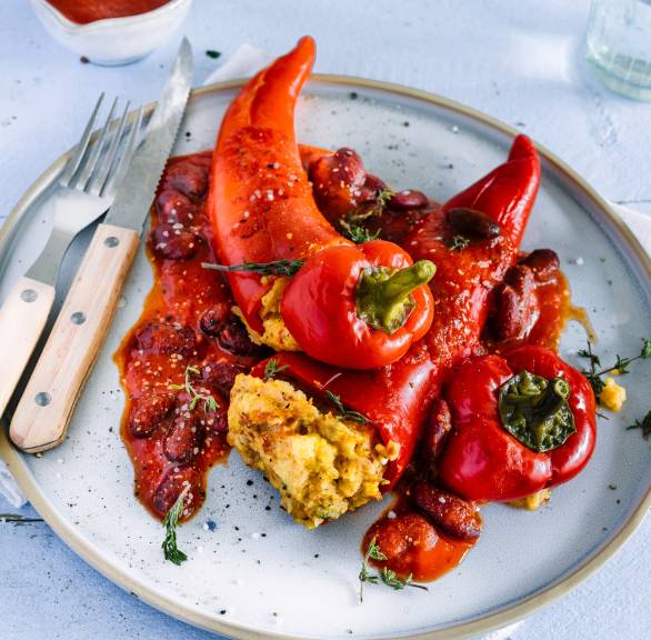Drei vegan gefüllte Spitzpaprikas mit Polentafüllung auf einem Teller getoppt mit Bohnensauce