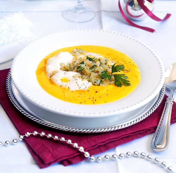 Goldene Apfel-Sellerie-Suppe in einem Suppenteller getoppt von Milchschaum und Jakobsmuschel-Tartar auf einem weihnachtlich dekorierten Tisch
