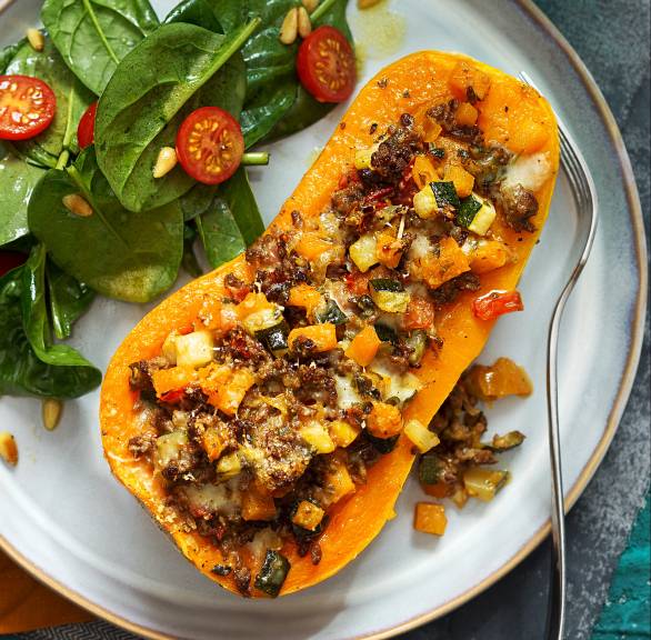 Halbierter Butternusskürbis auf einem Teller gefüllt mit Zucchini und Wurst