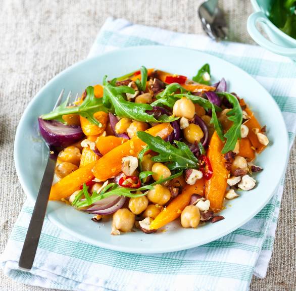 Karottensalat mir Kichererbsen und Rucola getoppt von Haselnüssen angerichtet auf einem Salatteller, daneben Vinaigrette