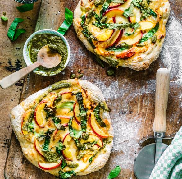 Pizza mit Nektarinen, Käse, Mangold und Pesto belegt auf einem Holzbrett