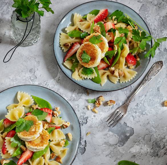 Nudelsalat mit Erdbeeren, Ziegenkäse und Zuckerschoten in einem tiefen Teller auf einem Tisch