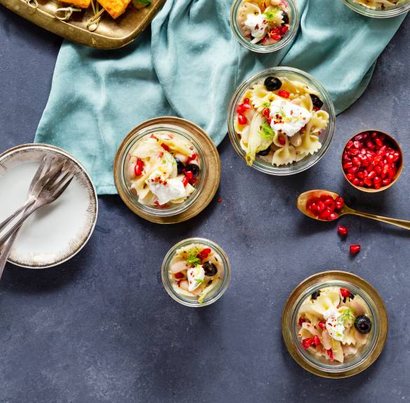 Nudelsalat aus Fusilli in Gläsern getoppt mit Ricotta und Granatapfelkernen auf einem Tisch