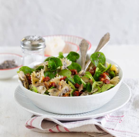 Nudelsalat aus Fusilli in einer Schüssel garniert mit Sardellen und getrockneten Tomaten