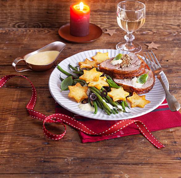 Gefüllter Putenrollbraten in Scheiben auf einem Teller, daneben Kartoffelsternen, grünen Bohnen und Zitronenschaum