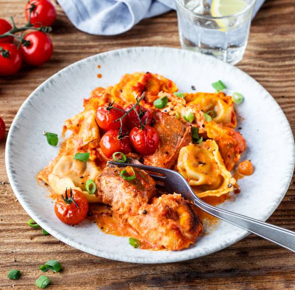 Ofenlachs und Tortellini in Tomaten-Sahne-Soße angerichtet auf einem Teller