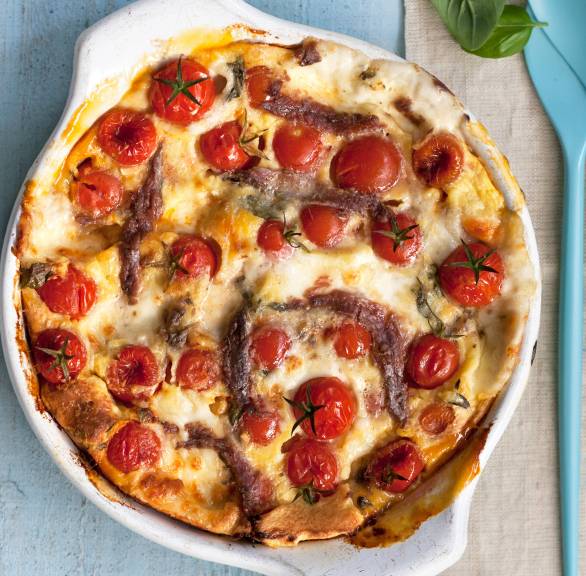 Ofenpfannkuchen in einer Auflaufform erkennbar sind Sardellen, Tomaten und Mozzarella