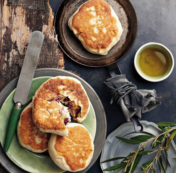 Fladenbrot in einer Pfanne, daneben drei weitere Brote auf einem Teller, eines aufgebrochen mit Olivenfüllung