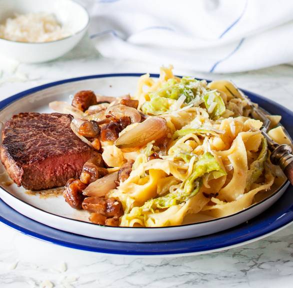 One-Pot-Bandnudeln auf einem Teller mit Wirsing und Soße, daneben Hüftsteak