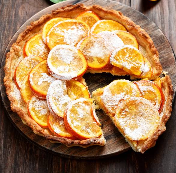Angeschnittene Crostata mit Haselnussboden und Vanillecreme-Füllung getoppt von kandierten Orangenscheiben auf einem Kuchenteller