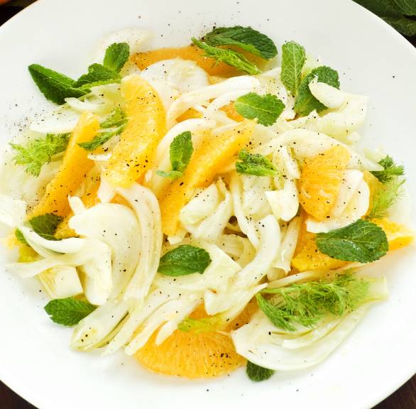 Fenchelsalat mit Orangen auf einem Teller, daneben Minze