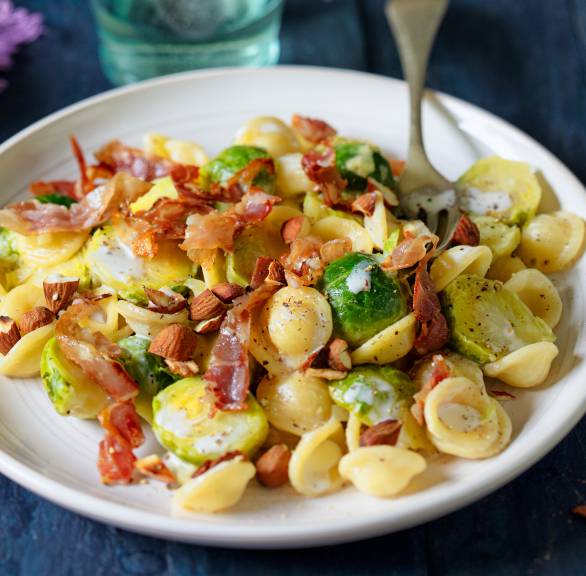 Orecchiette mit Rosenkohl und Pancetta getoppt von Mascarpone und Mandeln angerichtet auf einem Teller