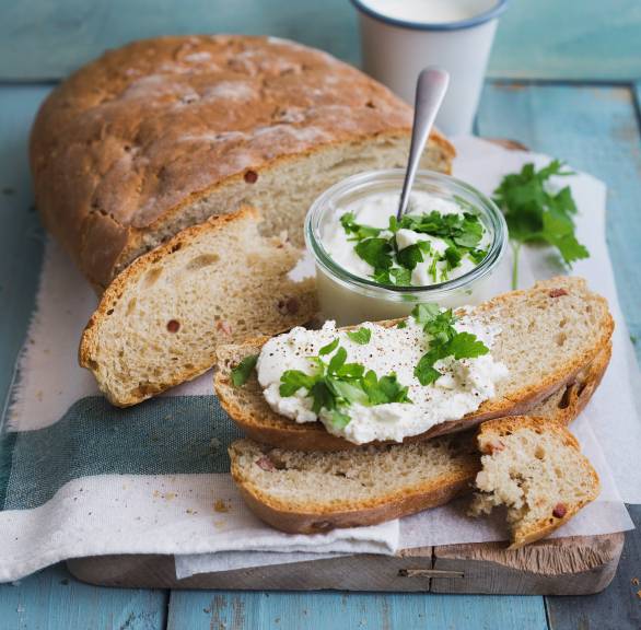 Kartoffelbrot angeschnitten auf einem Tisch, daneben einige Scheiben mit Joghurt-Dip und frischen Kräutern