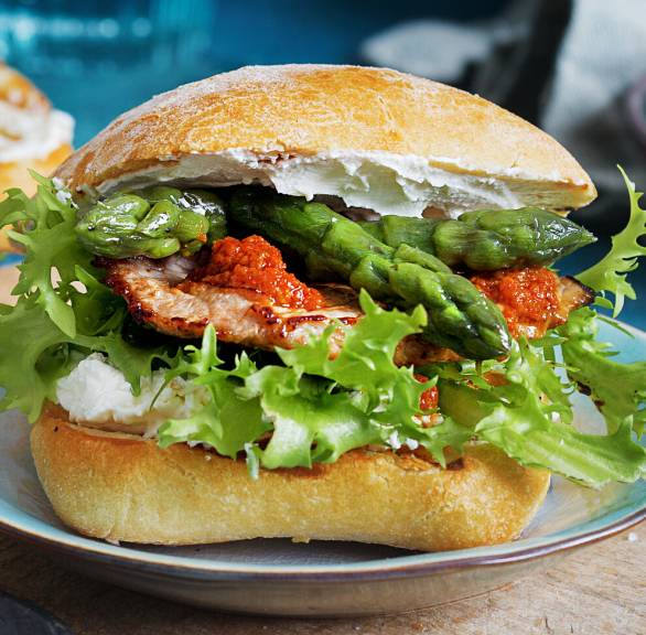 Belegtes Panini aus Ciabattabrötchen mit rotem Pesto, Spargel und Kalbsschnitzel auf einem Teller