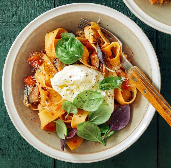 Pappardelle angerichtet mit Auberginensugo und getoppt von einer Burrata-Kugel auf einem Pastateller