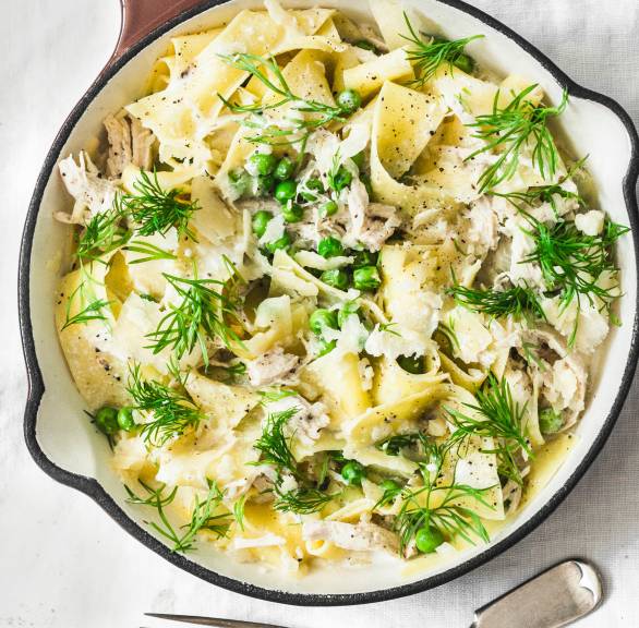 Pappardelle in einem Steiltopf getoppt mit Hähnchenragout, Erbsen und Fenchelgrün auf einem Tisch