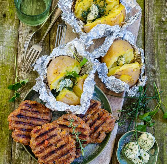 Mehrere Frikadellen mit Paprika und Mozzarella neben Backkartoffeln aus der Pfanne angerichtet auf einem Holzbrett